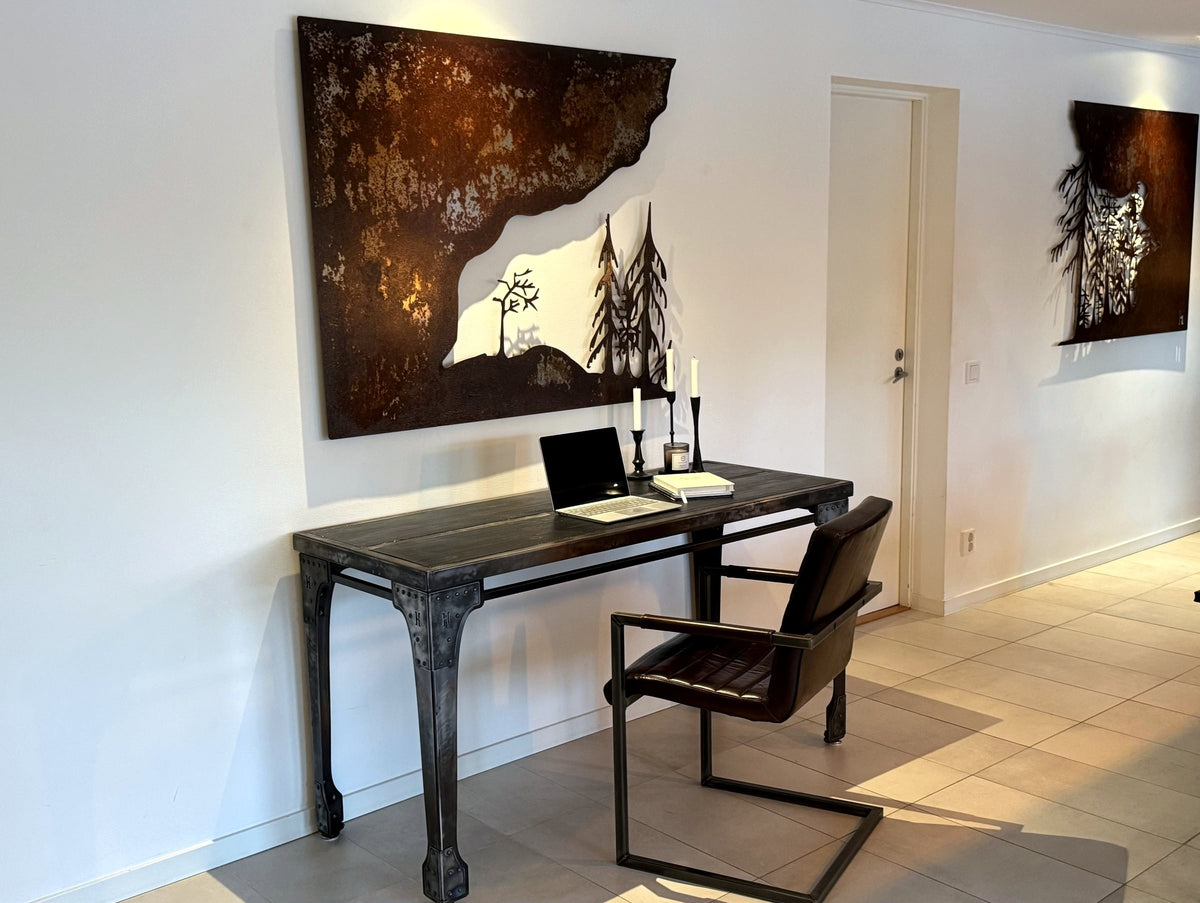 Stålskrivbord med brända träbrädor under en skogstavla i cortenstål, lodjurstavla i corten på väggen bredvid