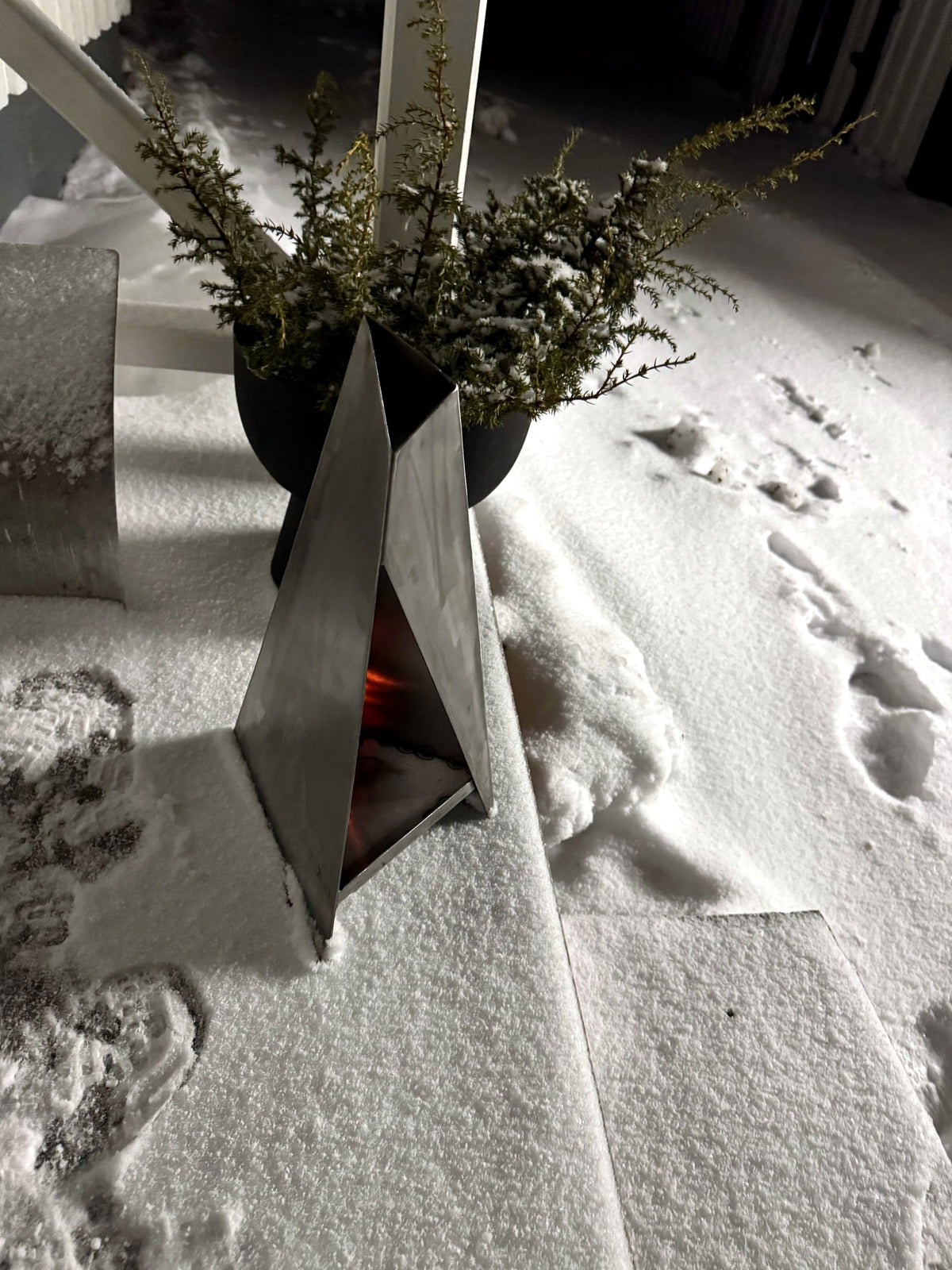 Triangel-ljuslykta tänd i snön en vinterkväll bredvid en kruka – här i blankt, obehandlat stål