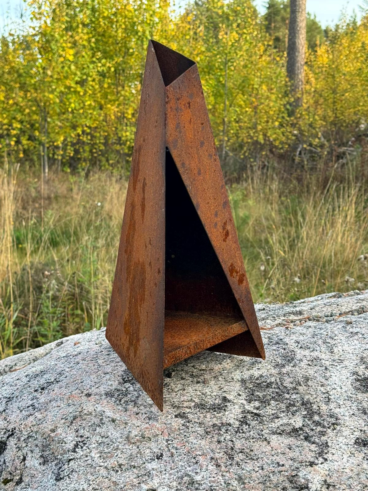 Triangel – ljuslykta i corten på sten med höstskog i bakgrunden