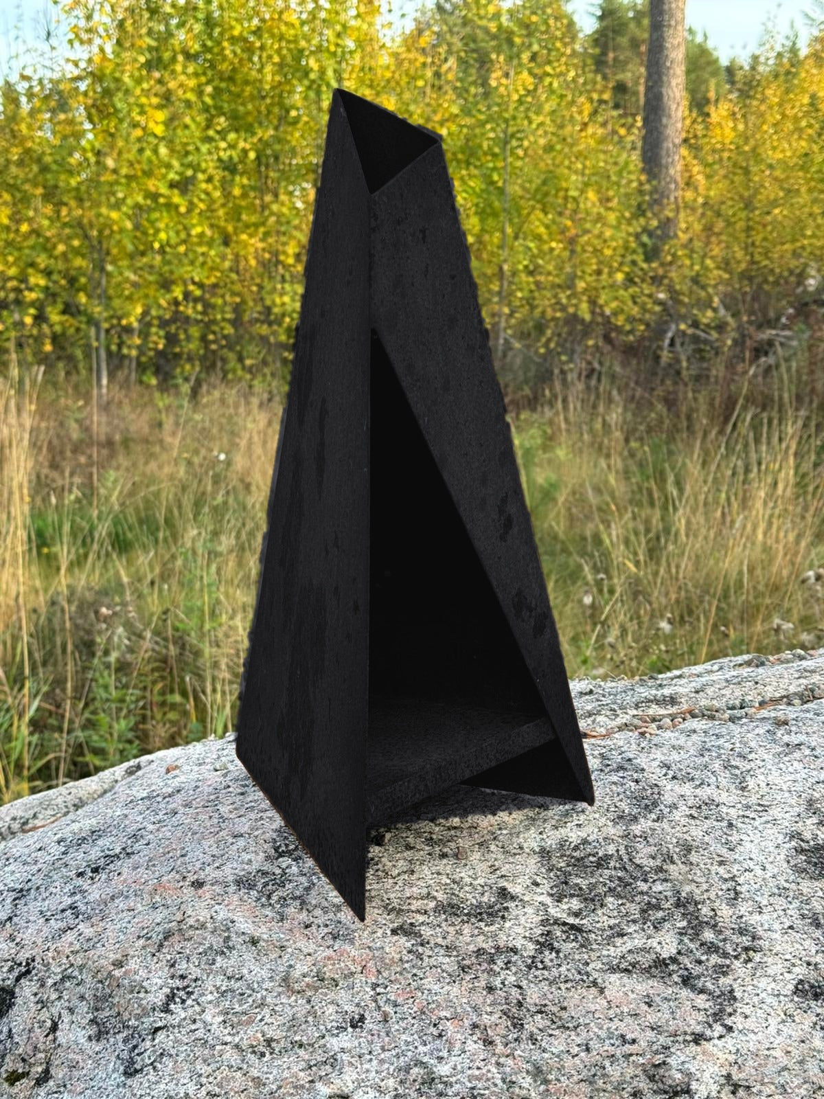 Svart Triangel-lykta på en sten med höstskog i bakgrunden